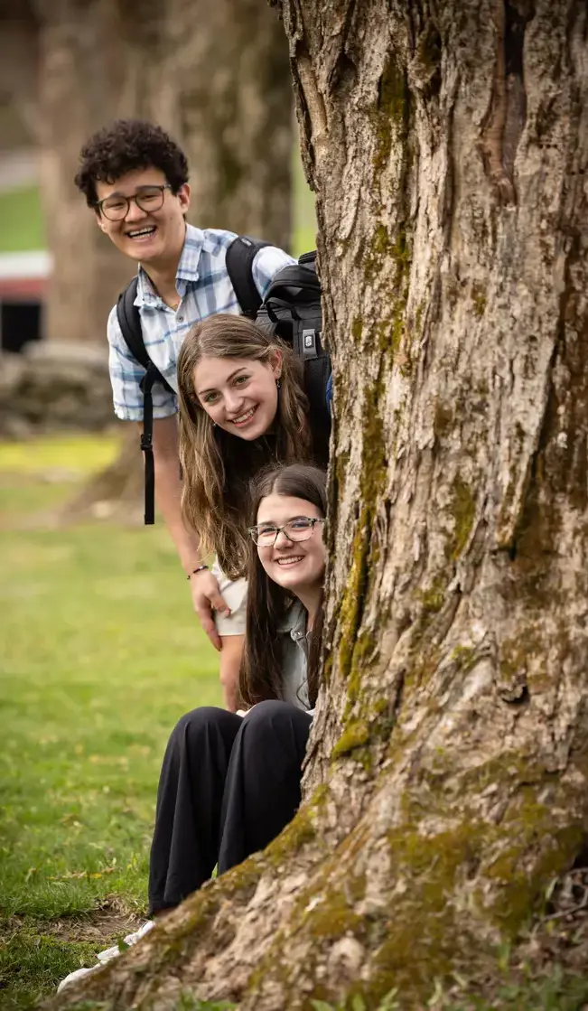 Students smiling and hiding behind tree