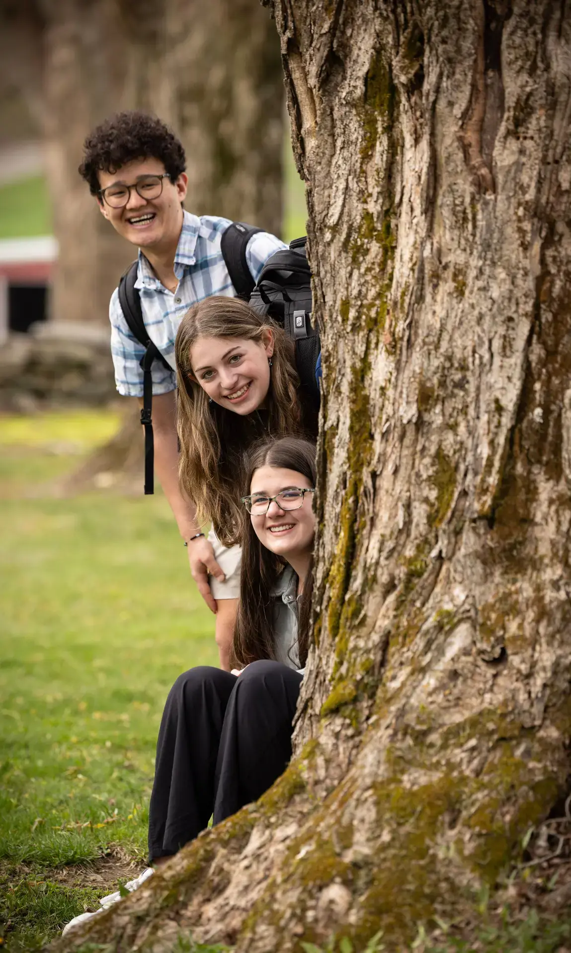 Students smiling and peeking from behind tree