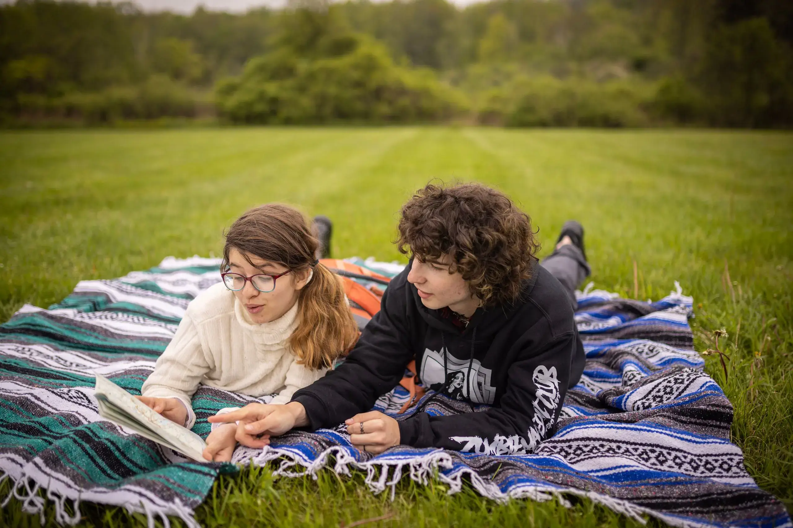 Students reading book together on picnic blanket in field