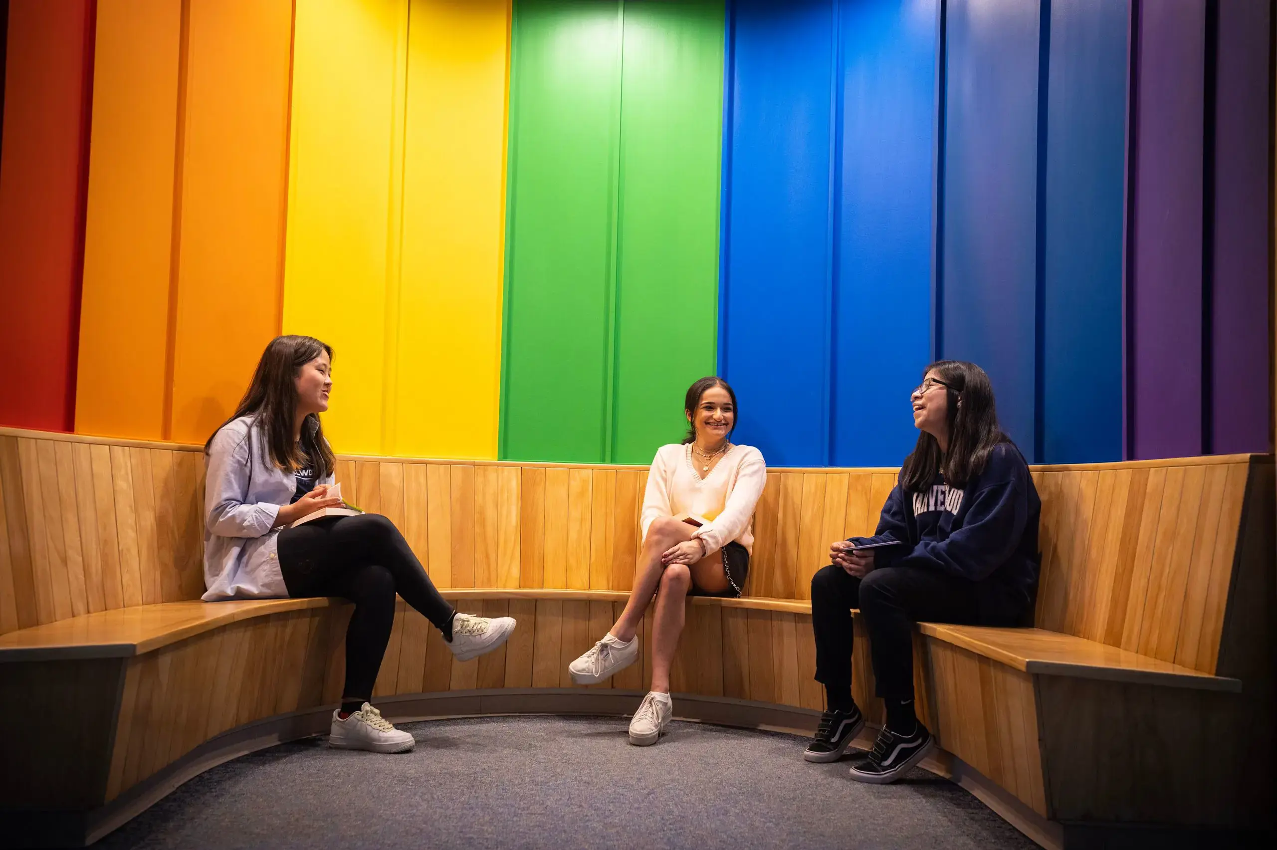 Students sat on bench with rainbow mural behind them